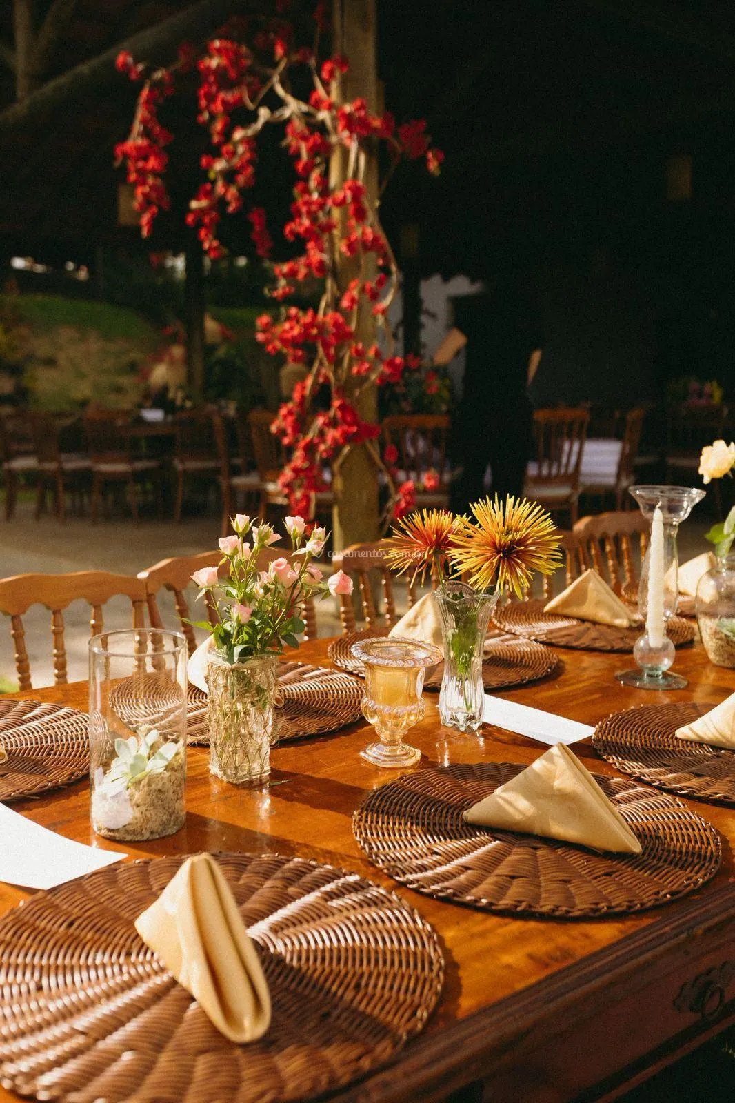 Flores vermelhas pendentes sobre mesa com sousplats de palha