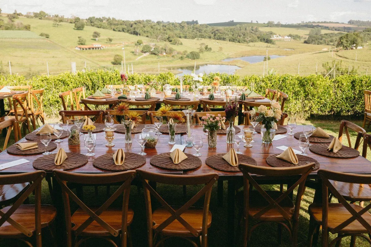 Mesa posta com sousplats de palha e flores, diante de um lago e das colinas verdes