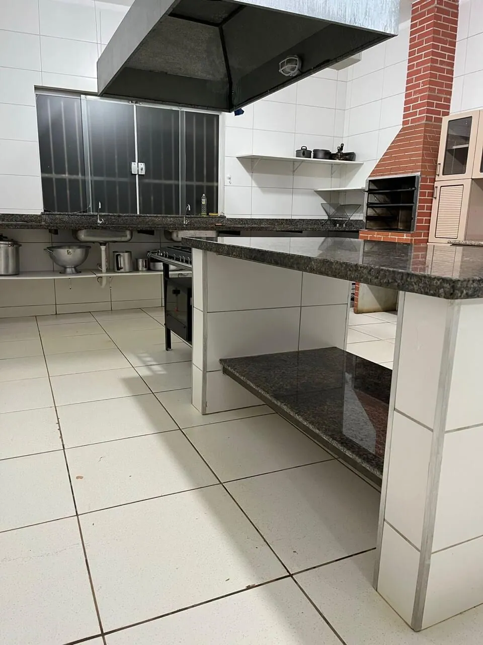 Cozinha de apoio com bancadas de granito, coifa e churrasqueira