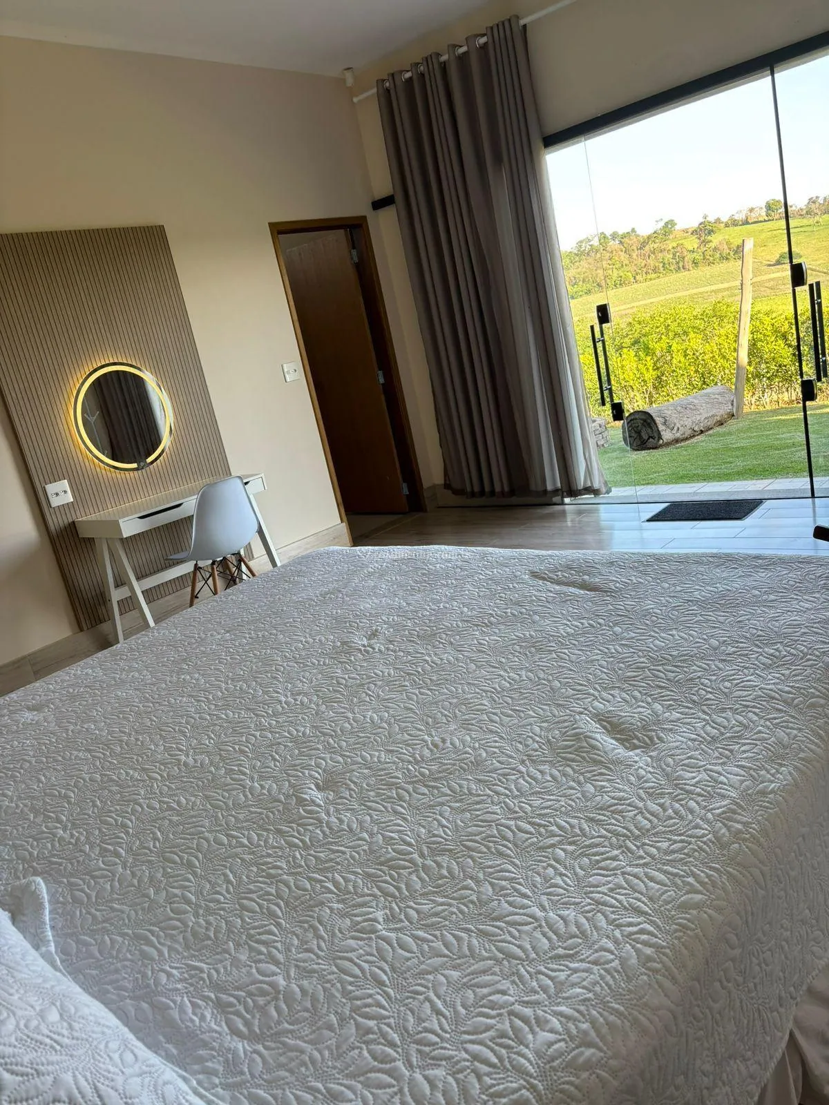 Suíte com cama de casal, penteadeira e porta de vidro aberta para o jardim